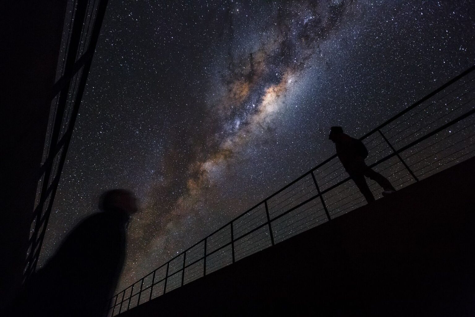 A person silhouetted against the Milky Way in a dark desert sky.