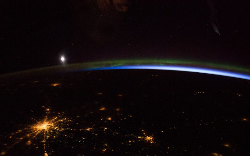 Earth at night from orbit with the aurora and the moon above the horizon.