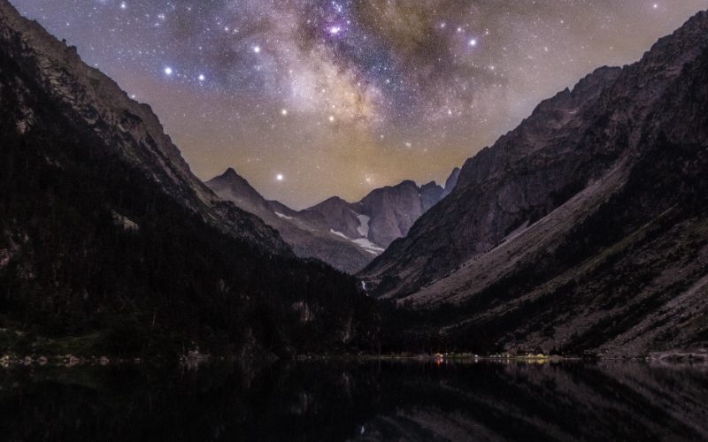 The Milky Way arching over a mountain lake at night.